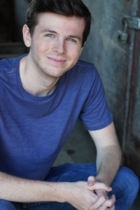 Headshot of Chandler Riggs. He is wearing a blue shirt and jeans, smiling at the camera.